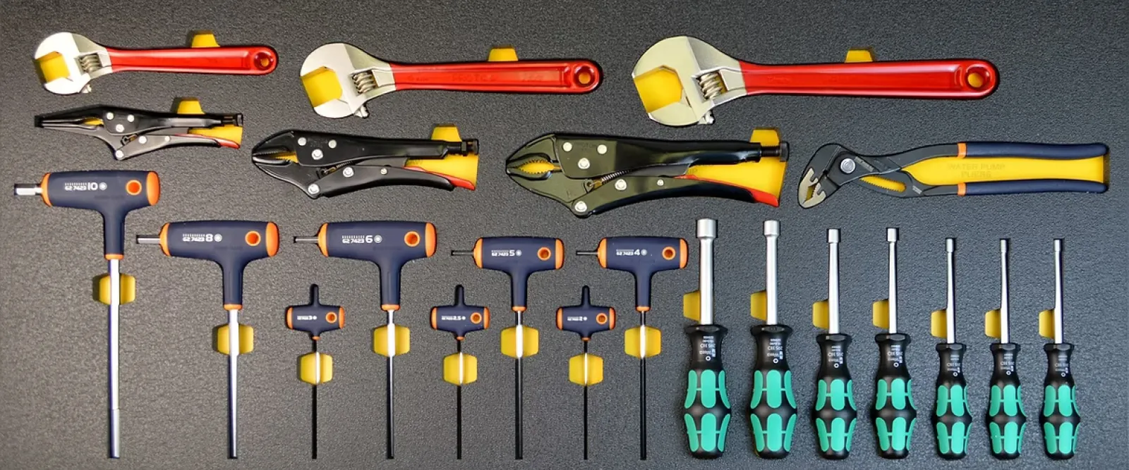Set of various hand tools including adjustable wrenches, locking pliers, T-handle hex keys, and screwdrivers organized on a gray surface.