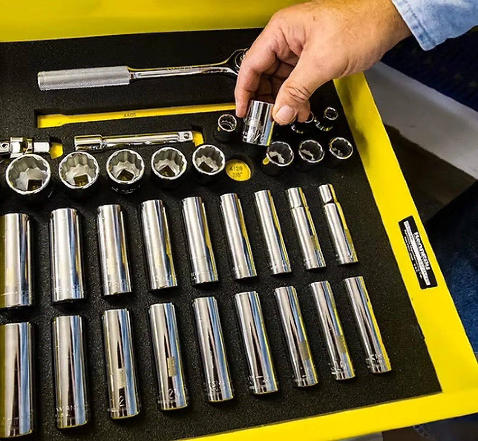 Person selecting a chrome socket from an organized tool tray with various socket sizes and wrench handles.