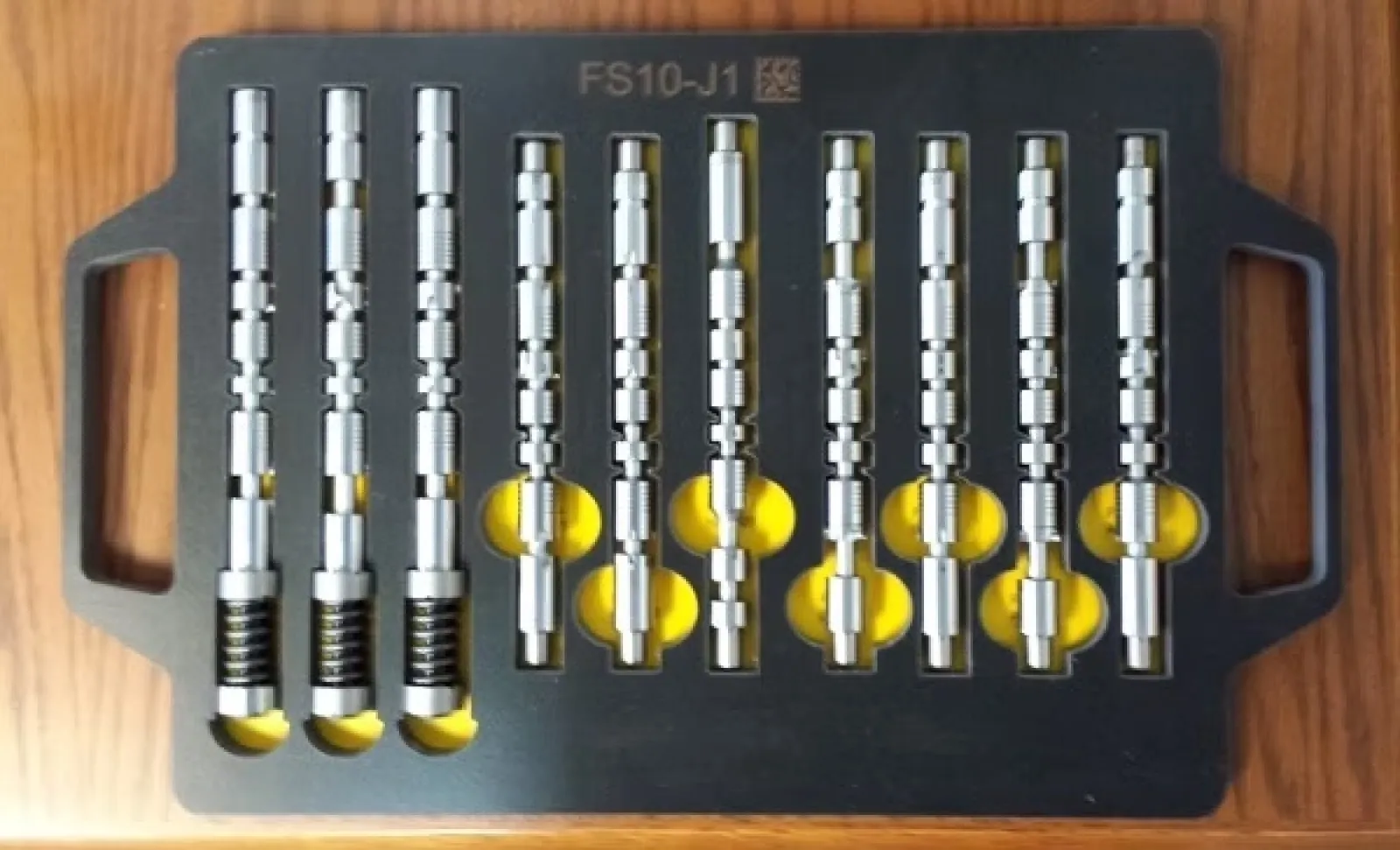 Set of metal lock pick tools with cylindrical shapes arranged neatly in a black tray on wooden surface.