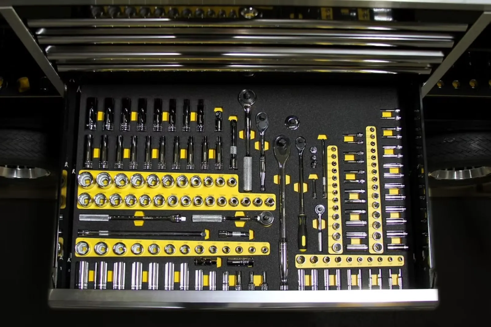 Open toolbox drawer with organized socket wrenches, ratchets, and various metal tools in yellow holders.