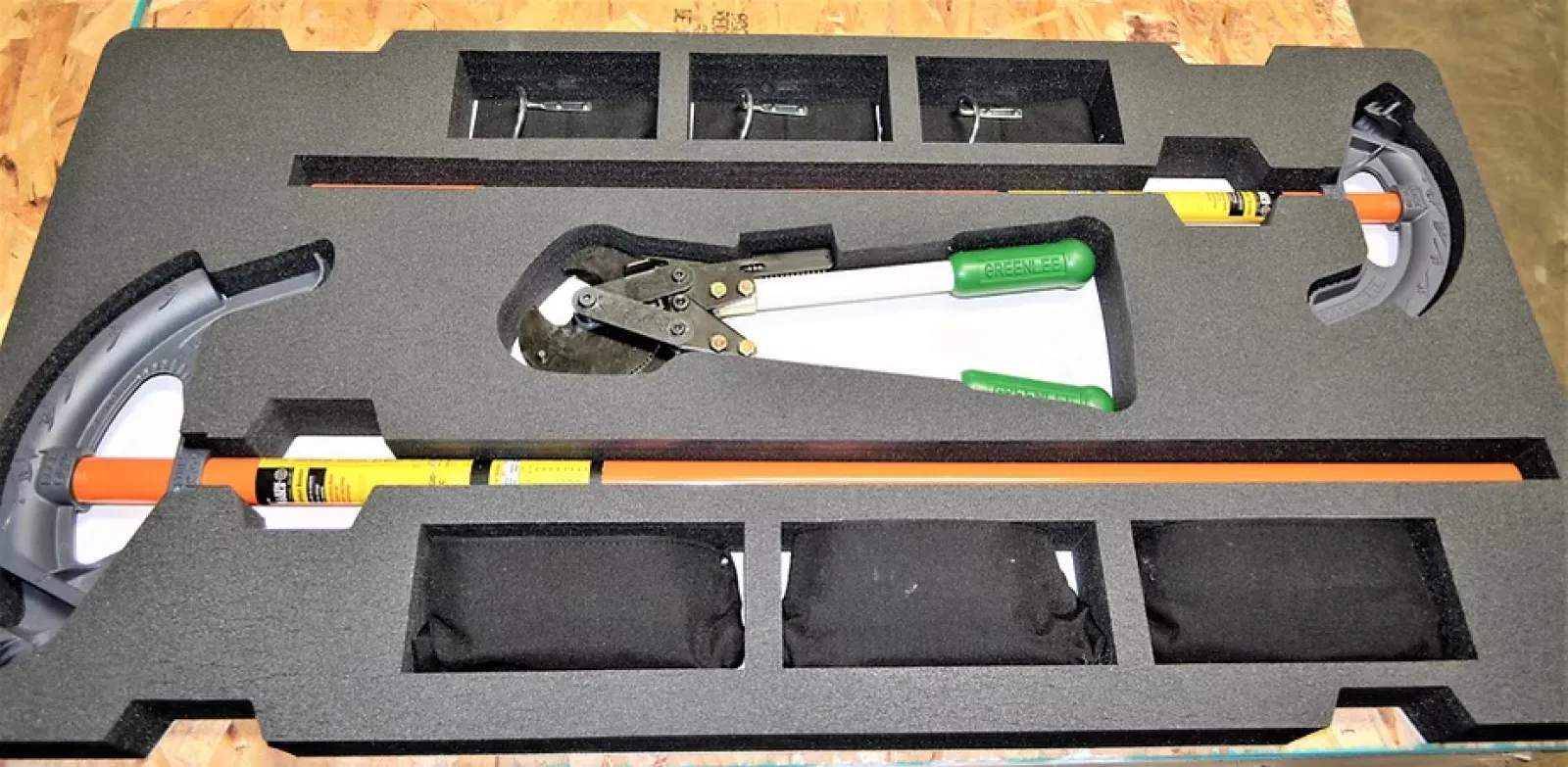Rescue tool kit in black foam casing with bolt cutters and two orange crowbars on wooden surface.