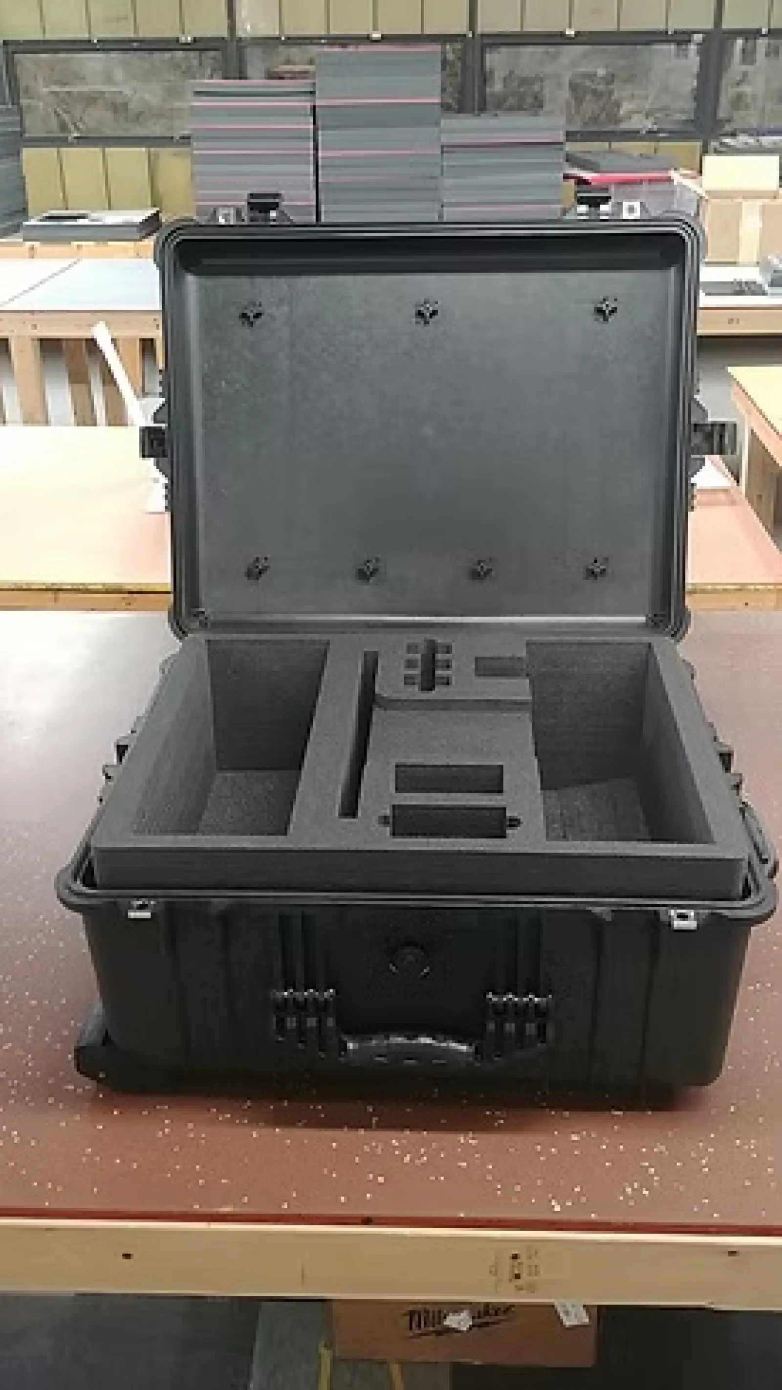 Open black hard case with custom foam compartments on a workbench in a workshop environment
