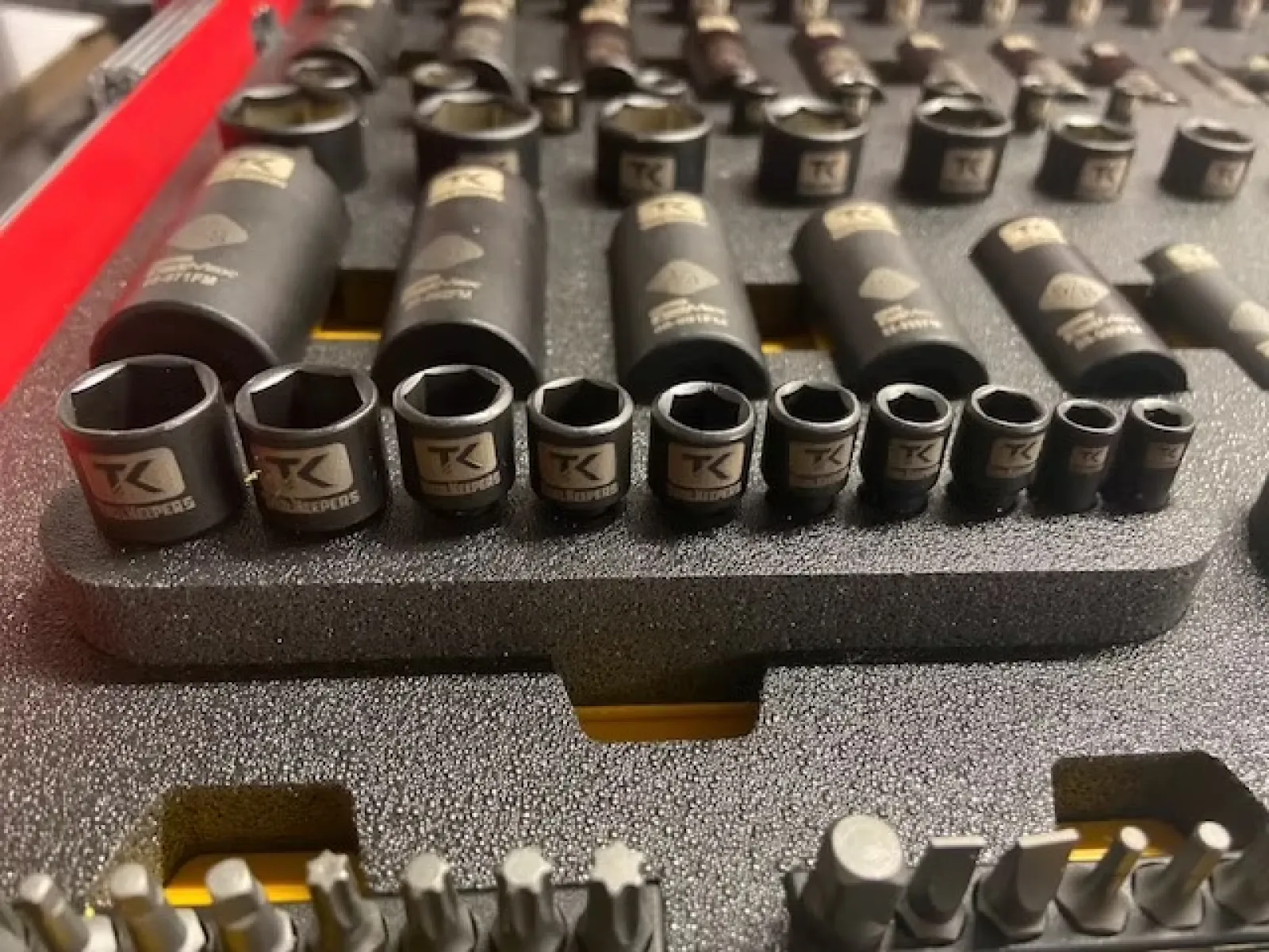 Close-up of a socket wrench set with various sizes neatly arranged in a foam tray, showing detailed TK branding.