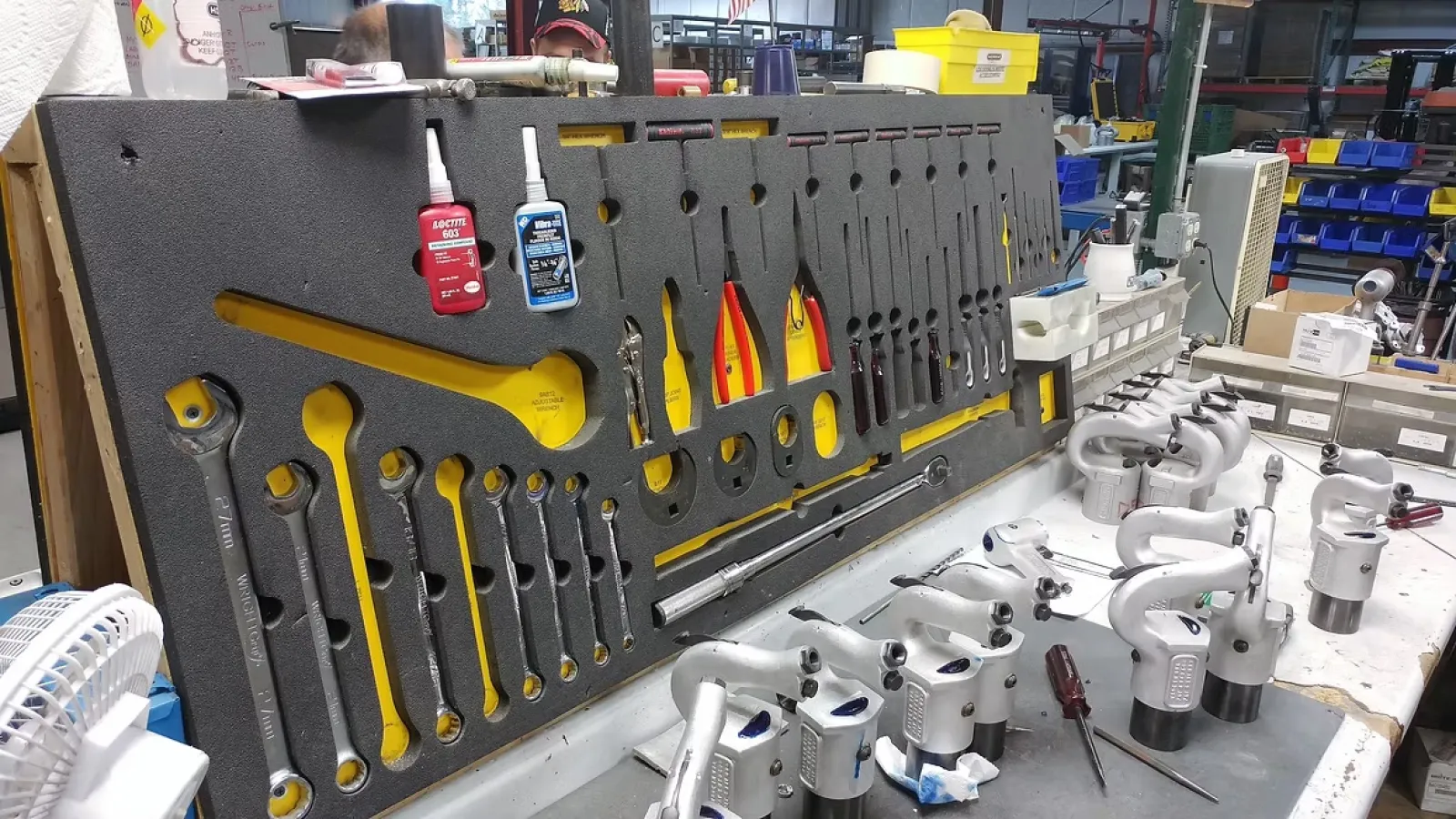 Organized workshop bench with various wrenches, hand tools, and piping equipment neatly arranged on foam board.