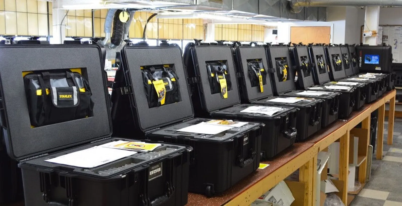 Row of black protective cases open on a workbench with papers inside an industrial workshop.