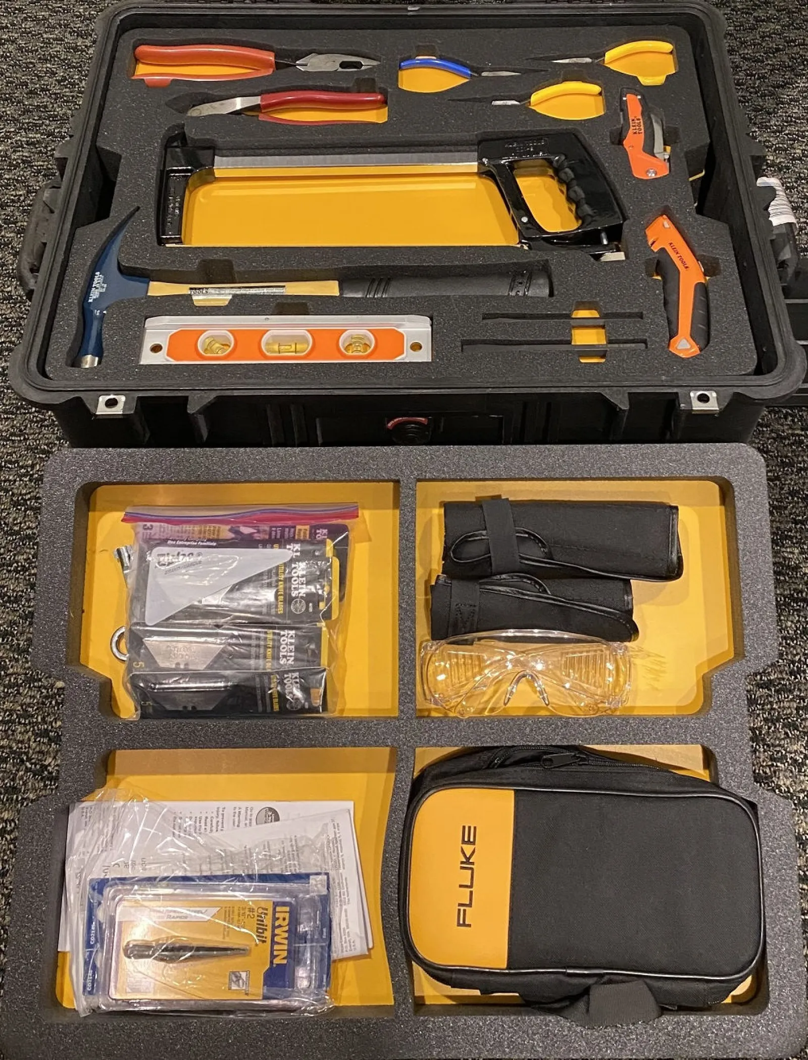 Organized toolkit case filled with hand tools, safety glasses, level, hammer, and Fluke branded bag on yellow foam insert.