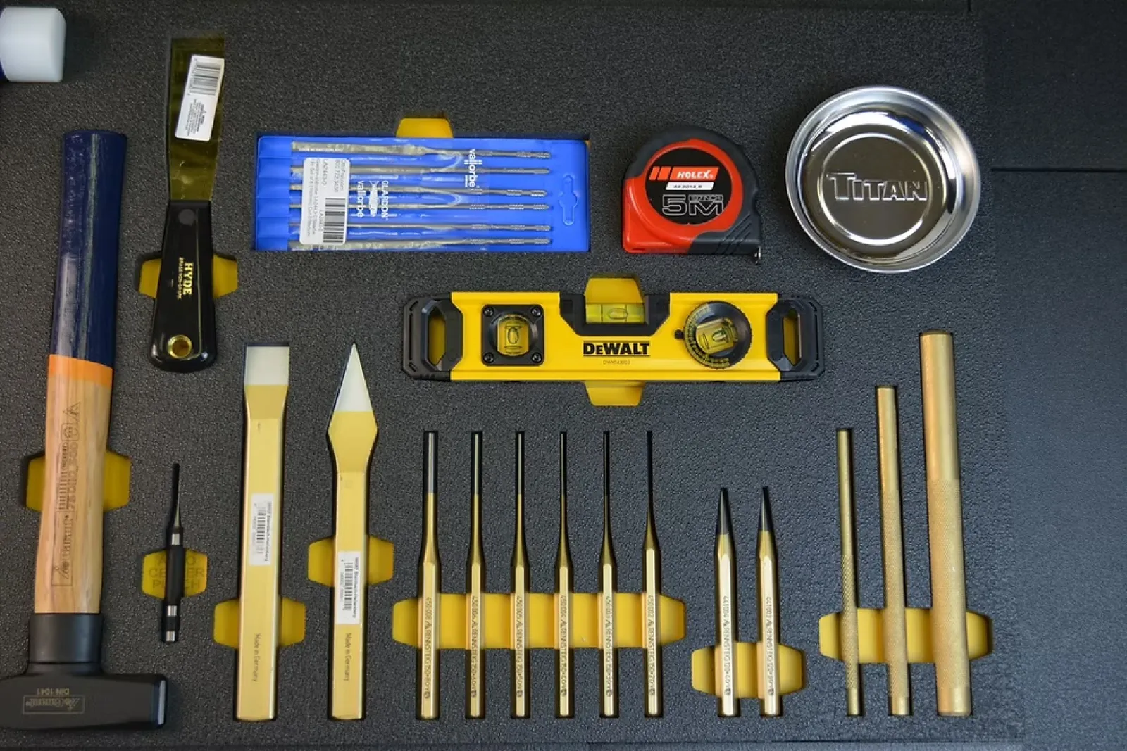 Set of precision hand tools including chisels, level, tape measure, and metal parts on black foam.