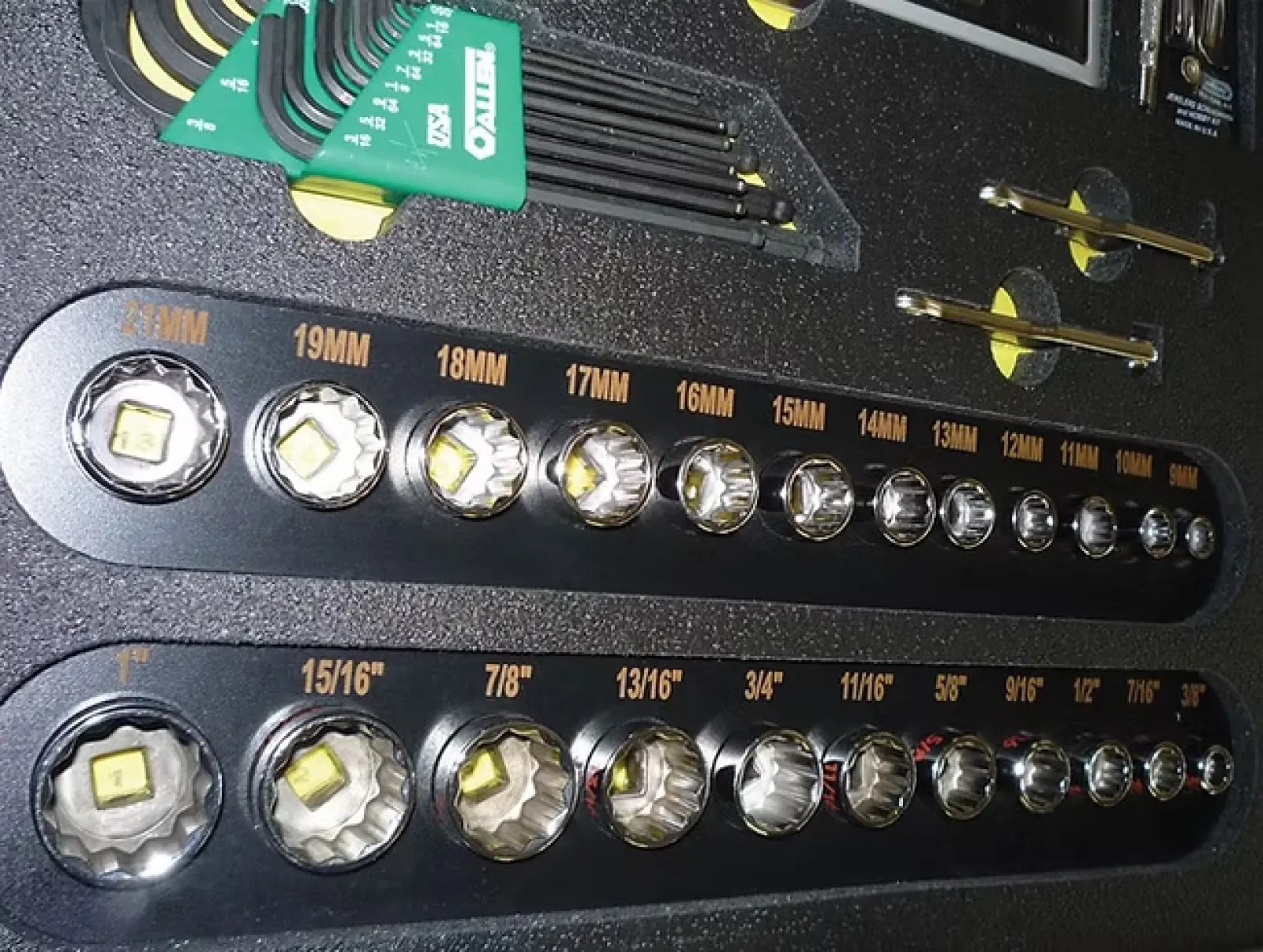 Set of various sized socket wrench heads and green hex keys in a black toolbox organizer.