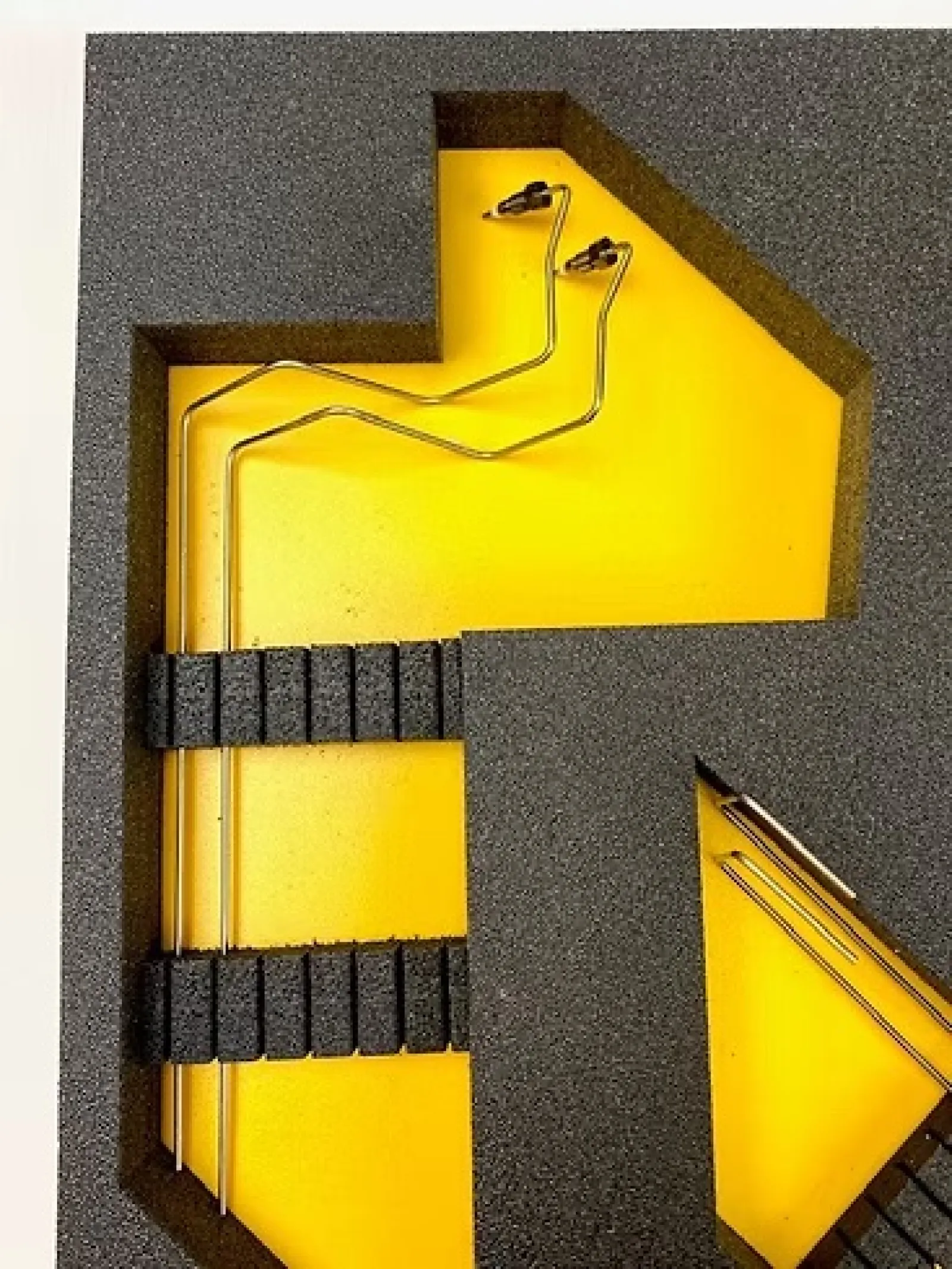 Black foam insert with yellow background holding metallic rods with black plastic ends in each slot.