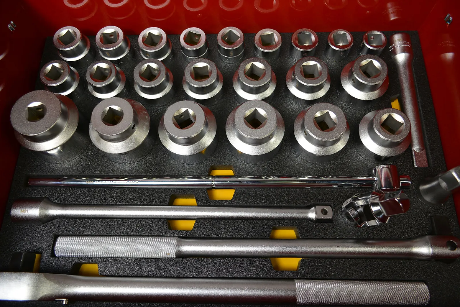 Set of heavy-duty metal socket wrenches and extension bars neatly arranged in a foam-lined red toolbox.
