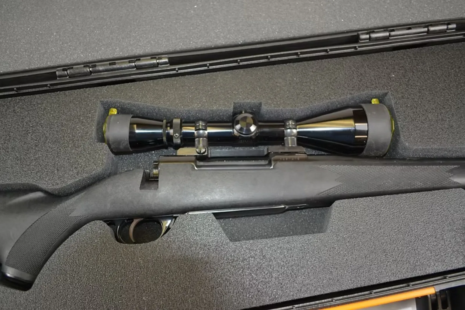 Black bolt-action rifle with mounted scope in protective foam rifle case for secure storage