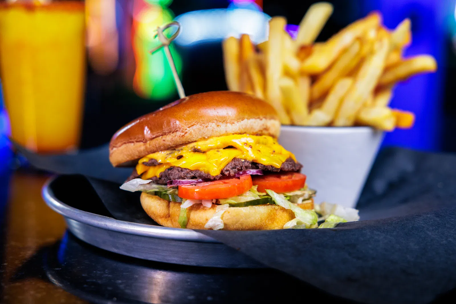 Juicy cheeseburger with lettuce, tomato, pickles, served with crispy fries and a drink in a colorful setting.