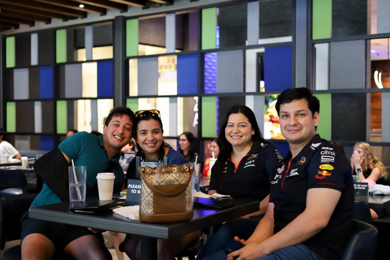 Four friends smiling together at a bustling café, enjoying drinks and each other's company.