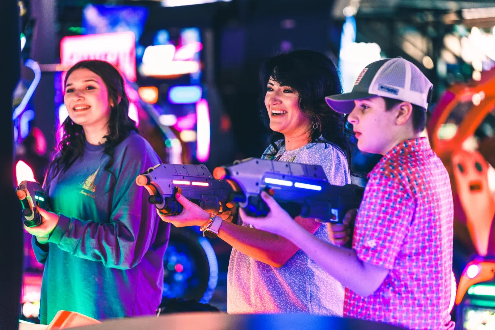 Three people playing laser tag with neon guns in a vibrant arcade environment at night.