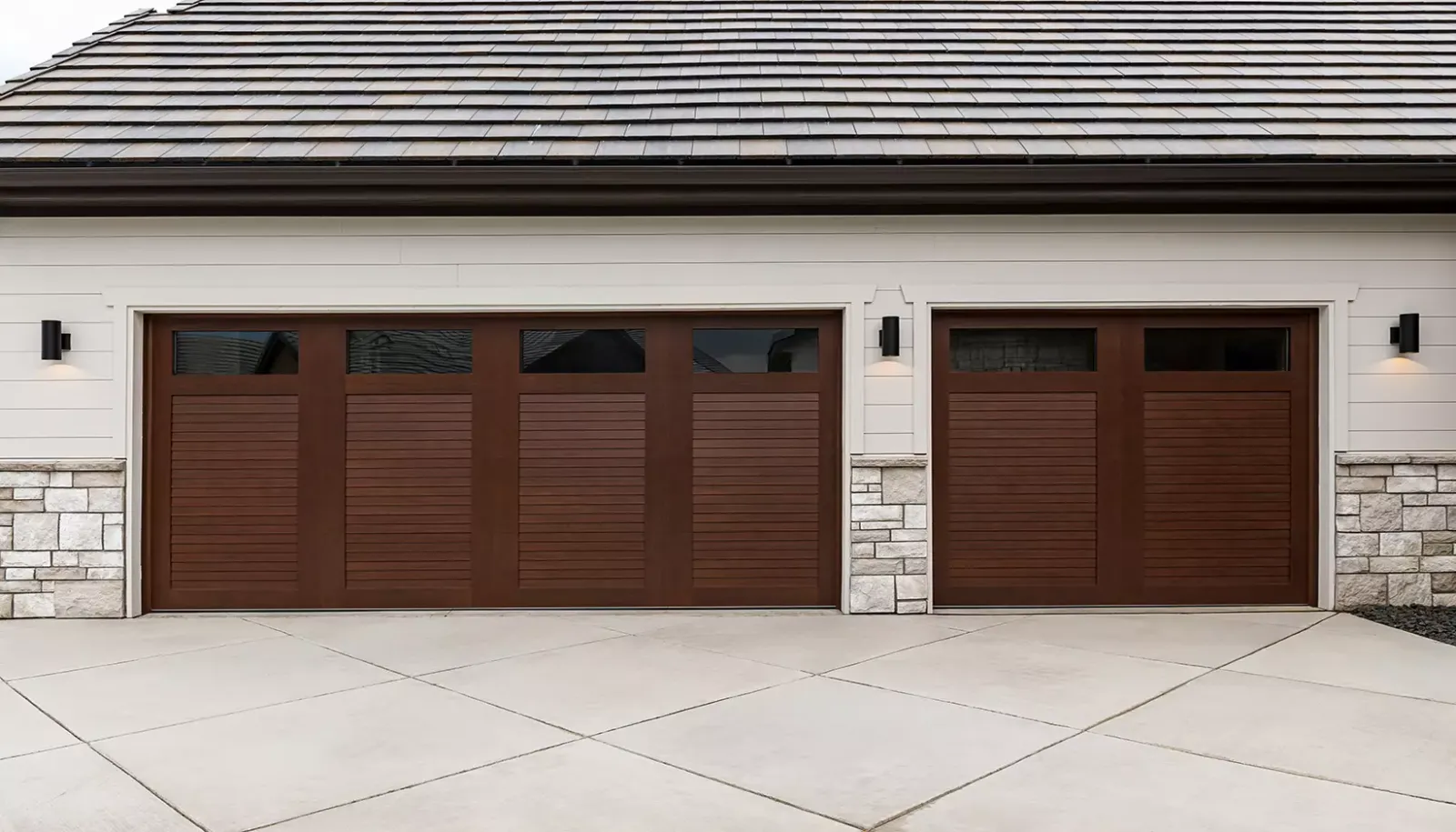 Modern house exterior with two dark wood panel garage doors on white siding and stone accents.