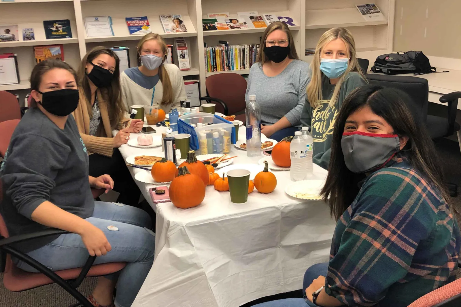 Students sit around a table painting pumpkins.