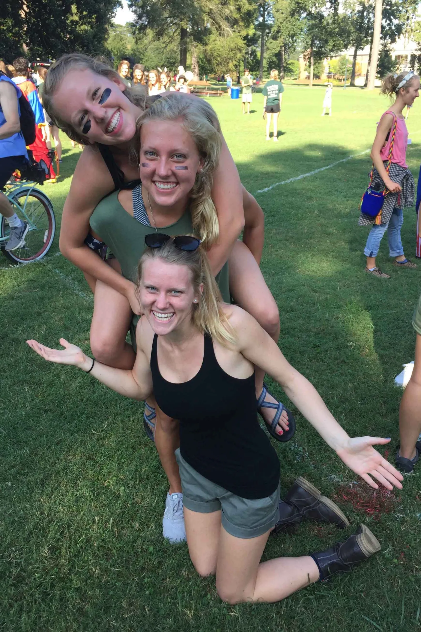 Three girls stand and kneel on the grass with a crowd behind them.