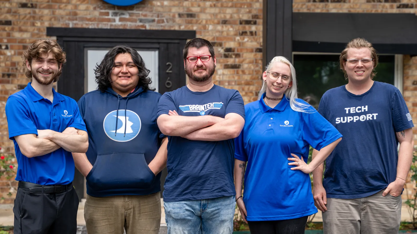 Five diverse tech support team members standing outdoors with arms crossed, smiling at the camera.