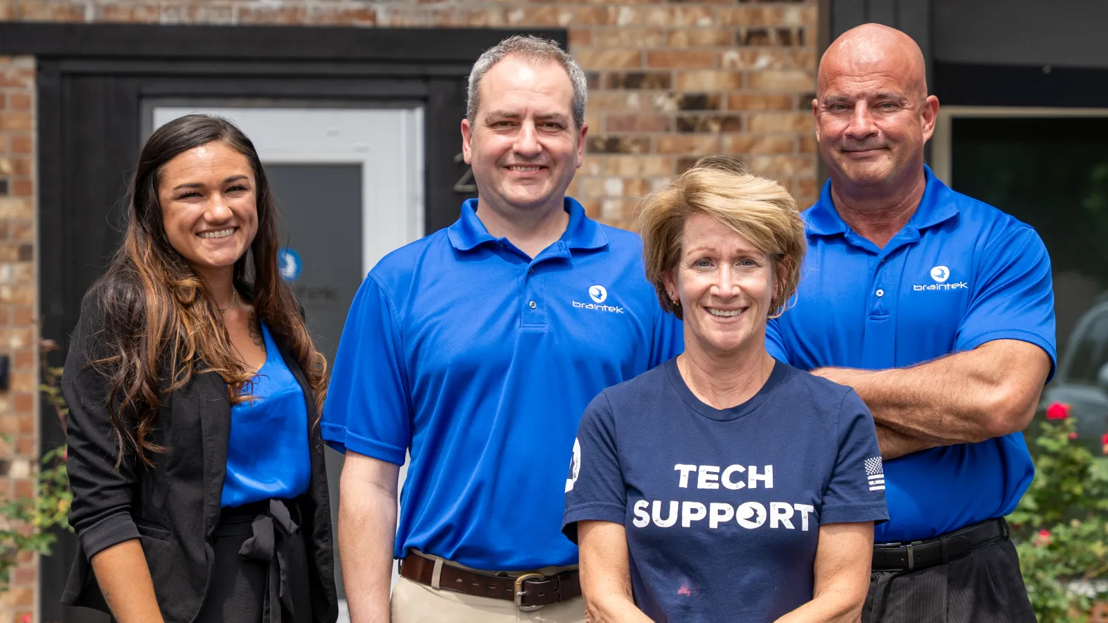 Smiling diverse tech support team standing outside office building in branded blue shirts and business attire.