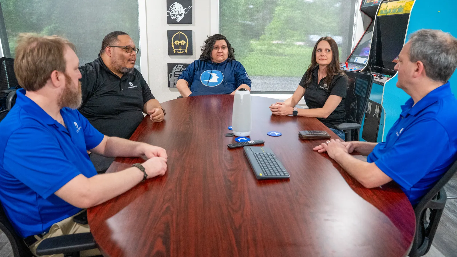 Five professionals engaged in a meeting around a wooden conference table in a modern office with natural light.