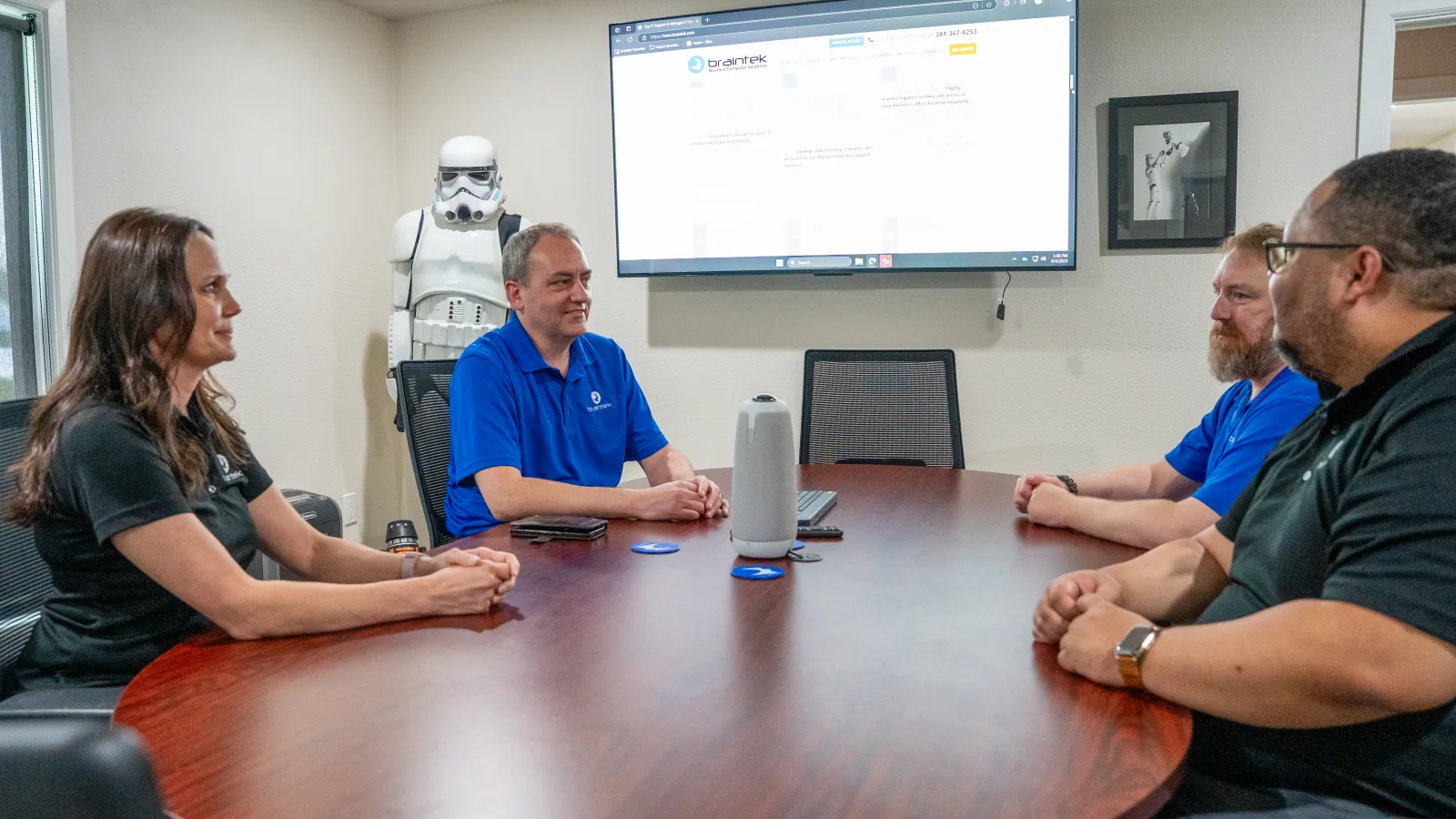 Four people having a discussion around a conference table with a screen and stormtrooper figure in the background