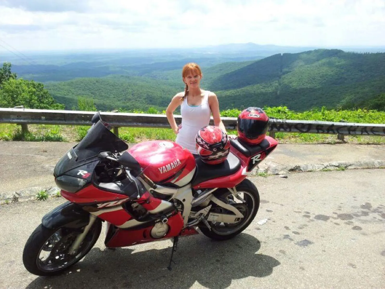 Jessi smiling next to a motorcycle parked on the side of a mountain