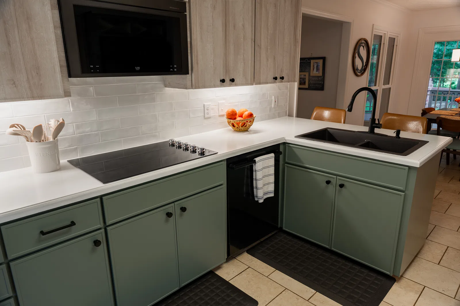 Modern kitchen with mint green cabinets, white countertops, black sink, stovetop, and fruit bowl on counter.