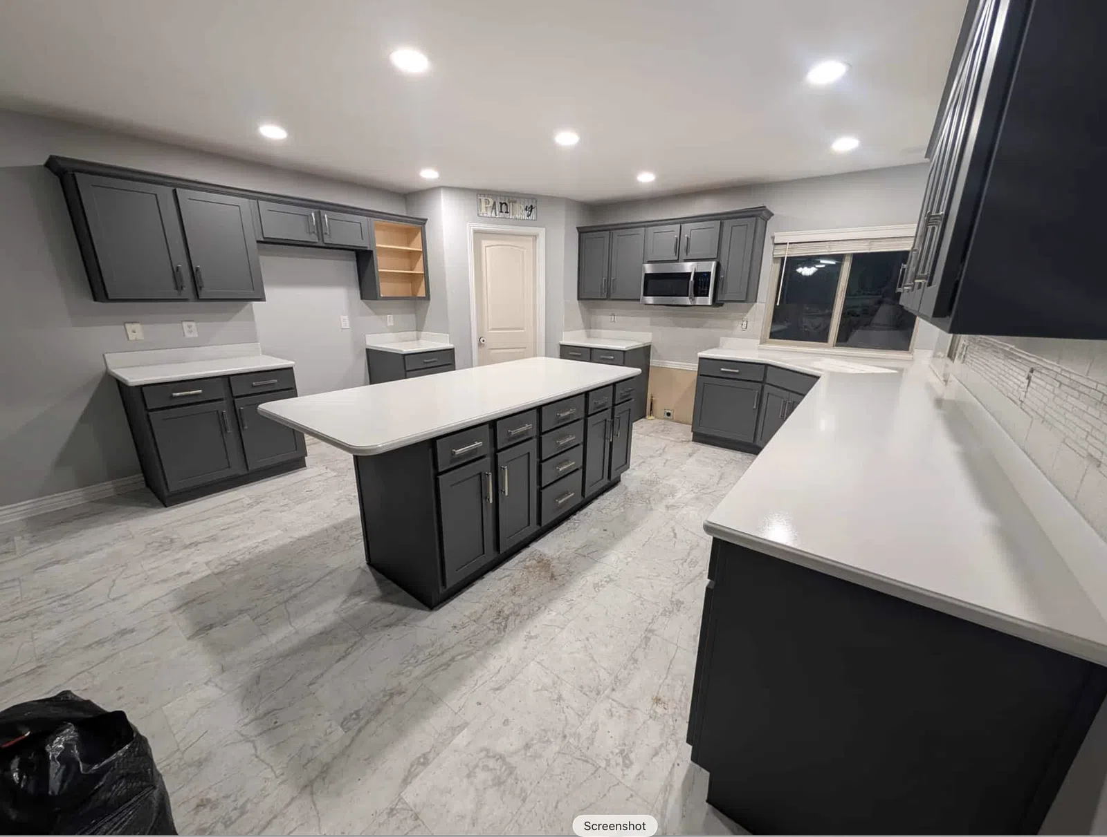 Modern kitchen with gray cabinets, white countertops, central island, and stainless steel microwave under bright lighting.