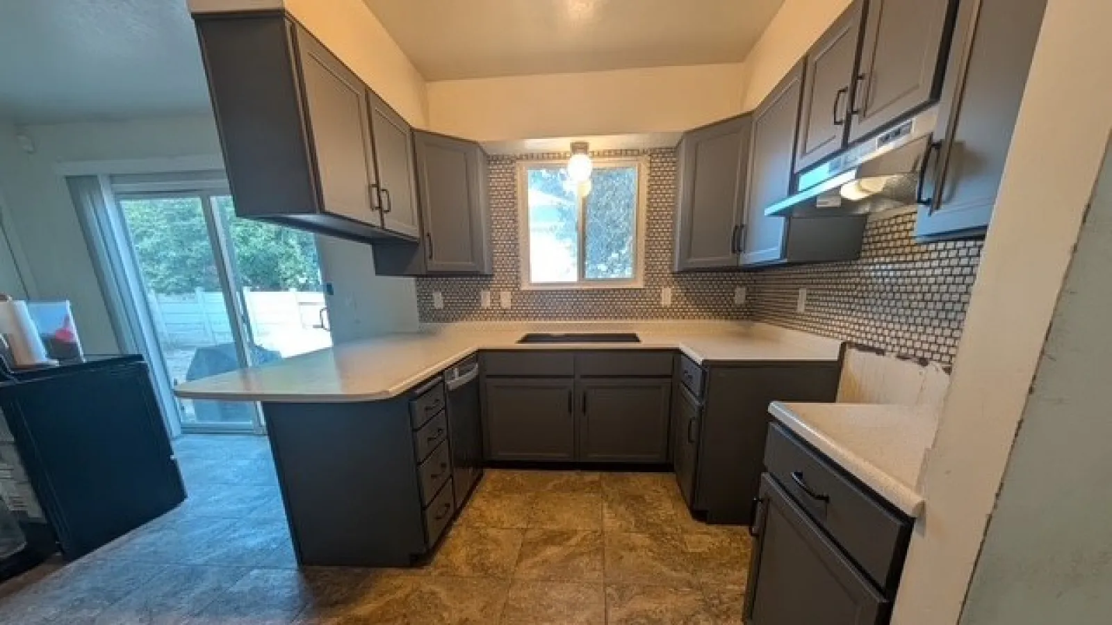 Modern kitchen with dark cabinetry, light countertops, tiled backsplash, and large sliding glass door to backyard.