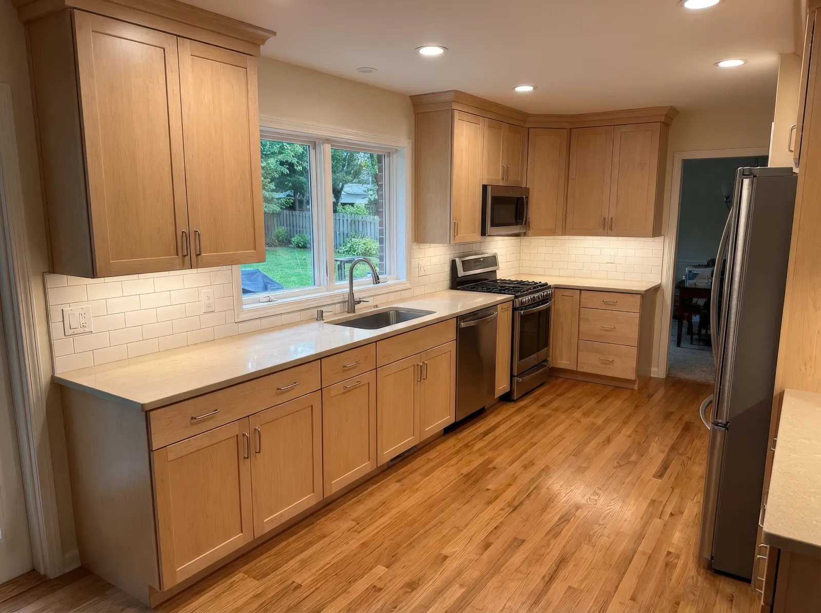 Bright modern kitchen with wooden cabinets, stainless steel appliances, white countertops, and hardwood floors.