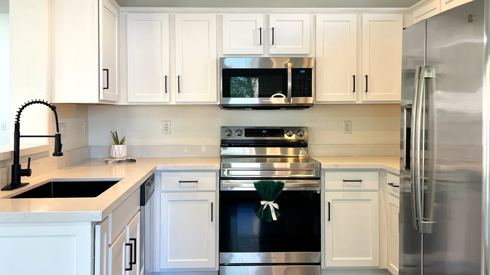 Modern kitchen with white cabinets, stainless steel appliances, wood flooring, black faucet, and recessed lighting.