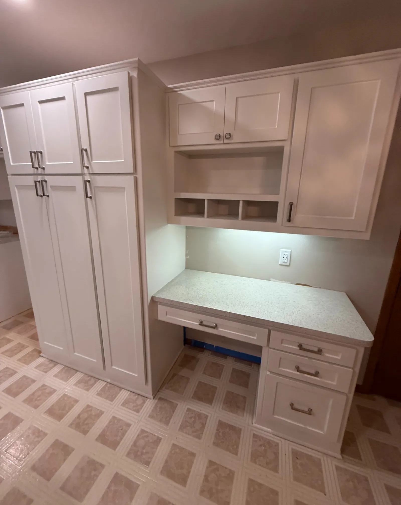 White kitchen cabinets and drawers with a countertop on patterned tiled floor in bright lighting.