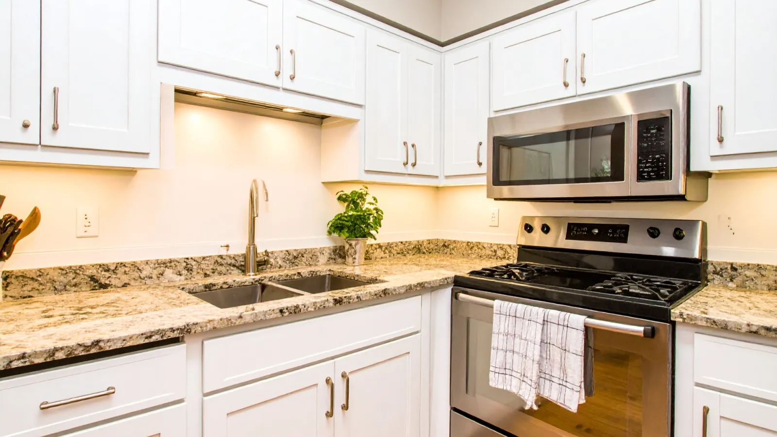 Modern kitchen with white cabinets, granite countertops, stainless steel stove and microwave, double sink.