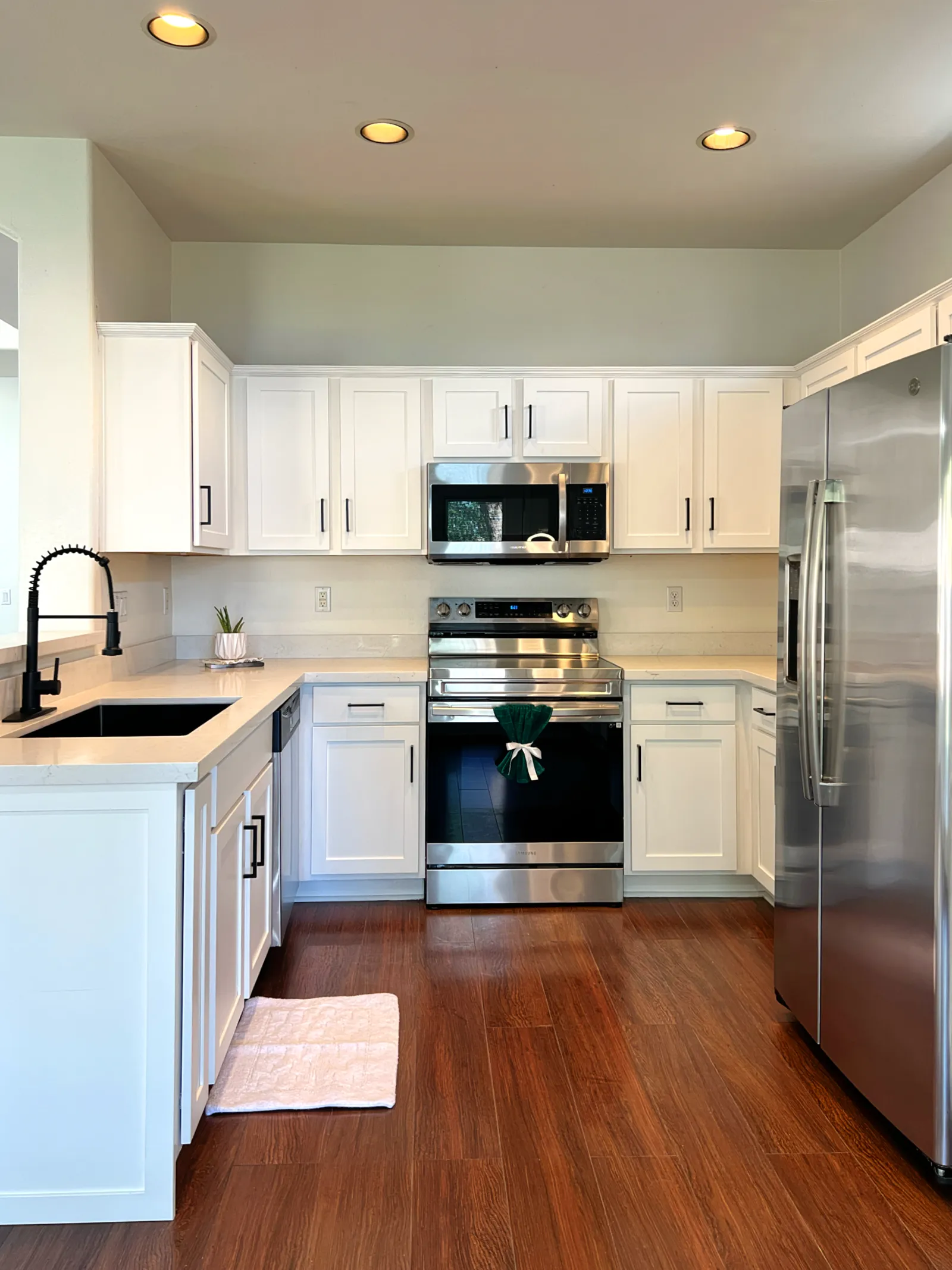 Modern kitchen with white cabinets, stainless steel appliances, dark wood floor, and black faucet on sink.