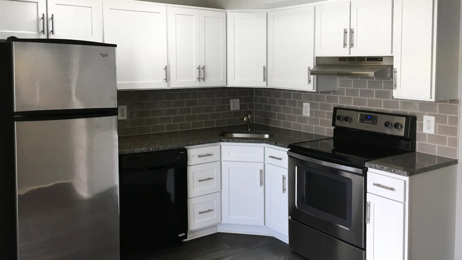 Modern kitchen corner with white cabinets, stainless steel fridge and oven, black dishwasher, and gray subway tile backsplash.