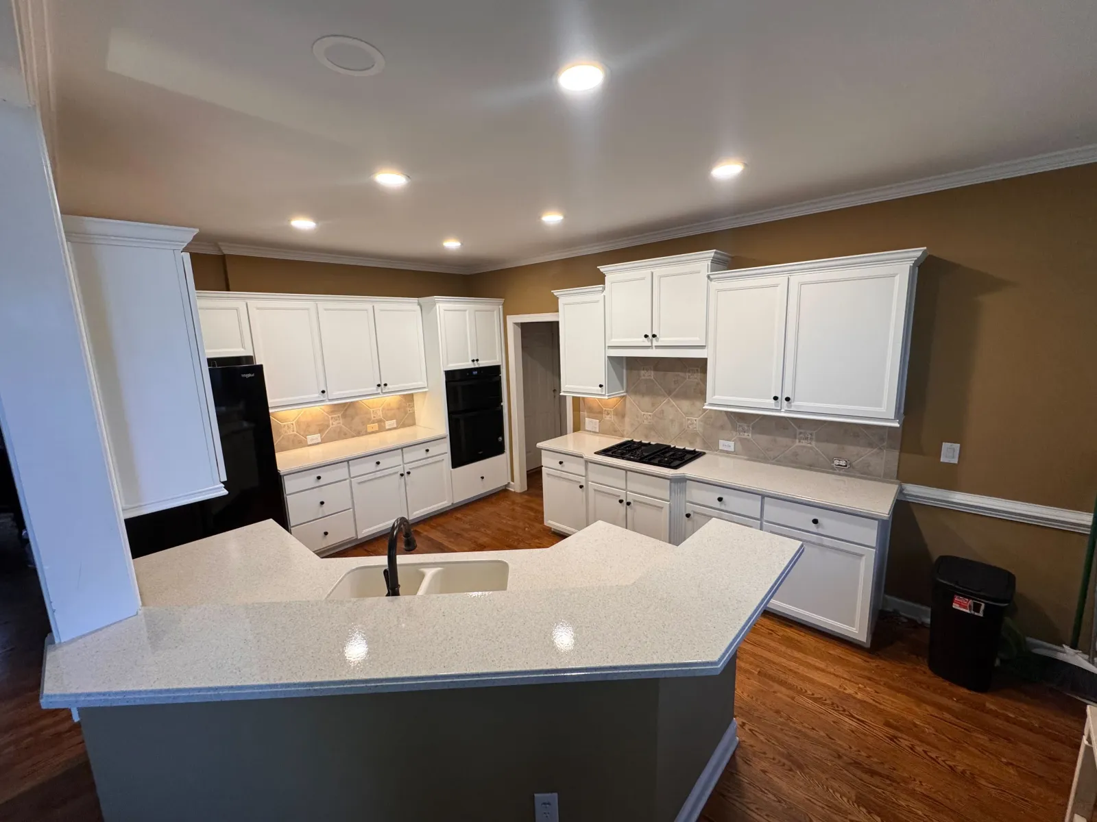 Modern kitchen with white cabinets, beige countertops, hardwood floors, and recessed lighting fixtures.
