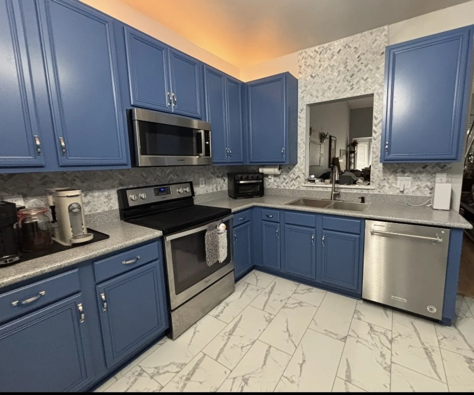 Modern kitchen with blue cabinets, stainless steel appliances, gray countertops, marble tile floor, and textured backsplash.