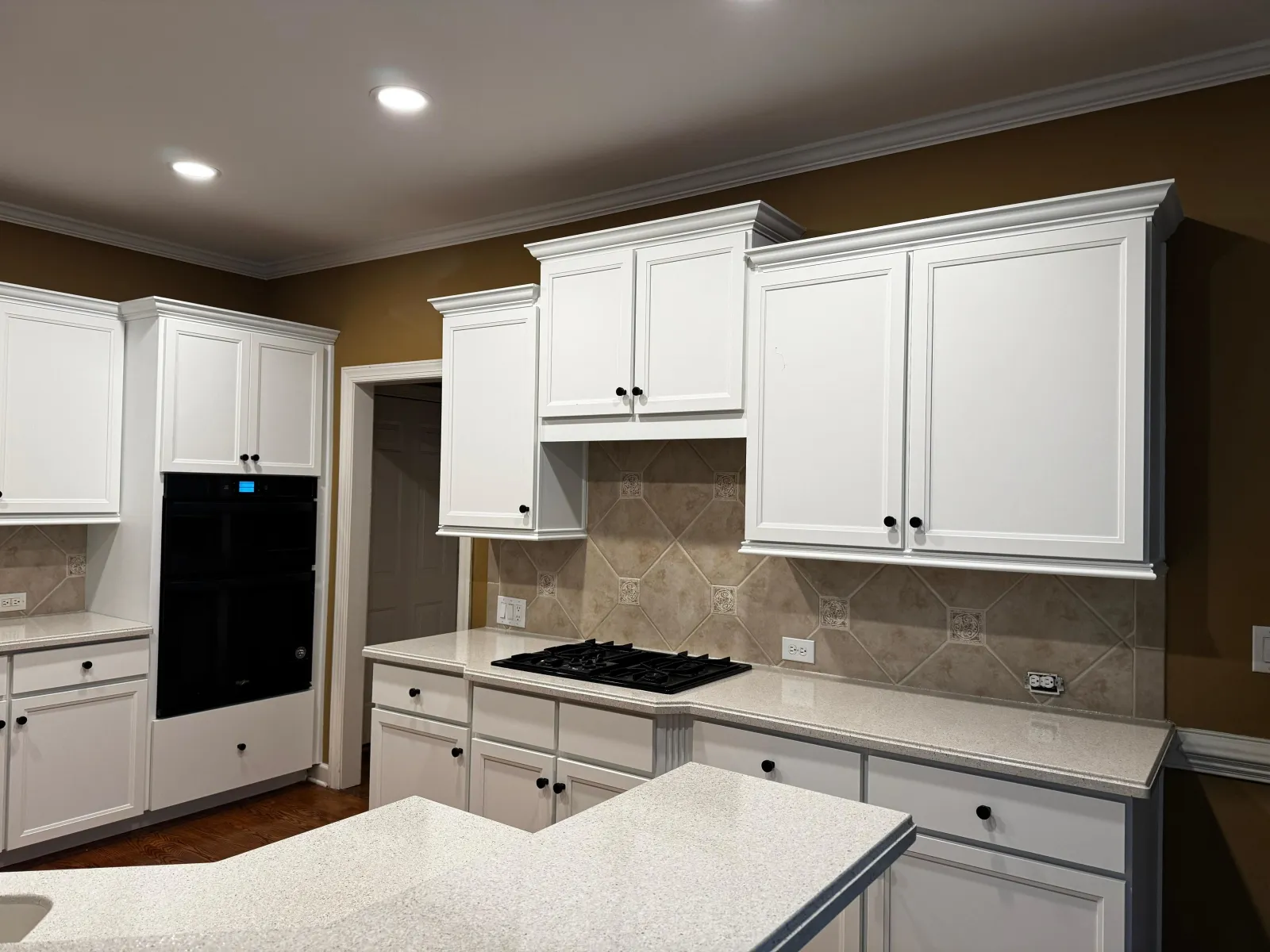 Modern kitchen with white cabinets, beige tiled backsplash, black stove, and glossy quartz countertops under recessed lighting