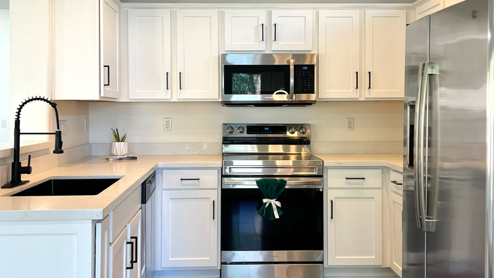 Modern kitchen with white cabinets, stainless steel appliances, wood flooring, black faucet, and recessed lighting.