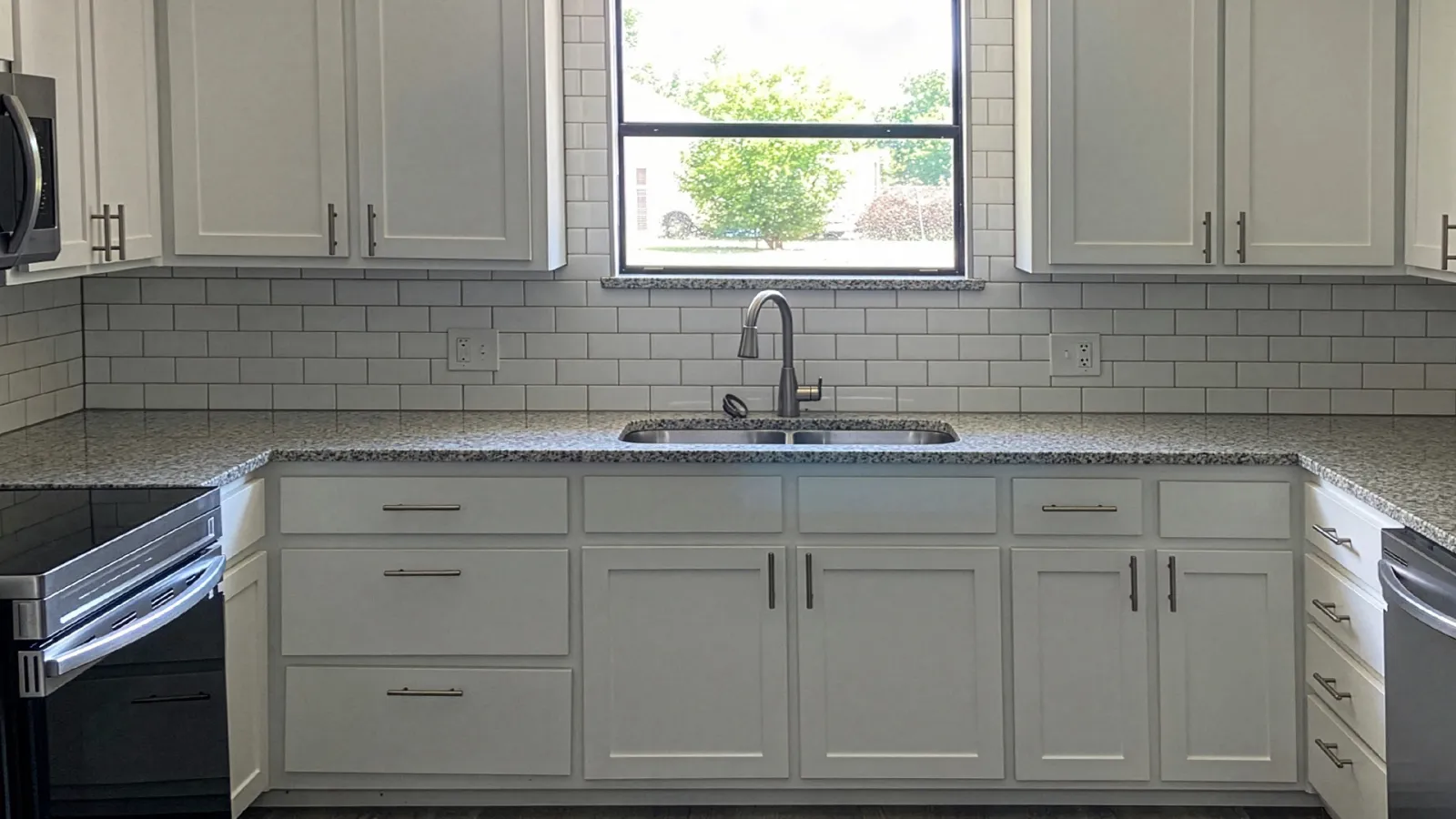 Modern kitchen with white cabinets, granite countertops, subway tile backsplash, stainless steel appliances, and a window above the sink