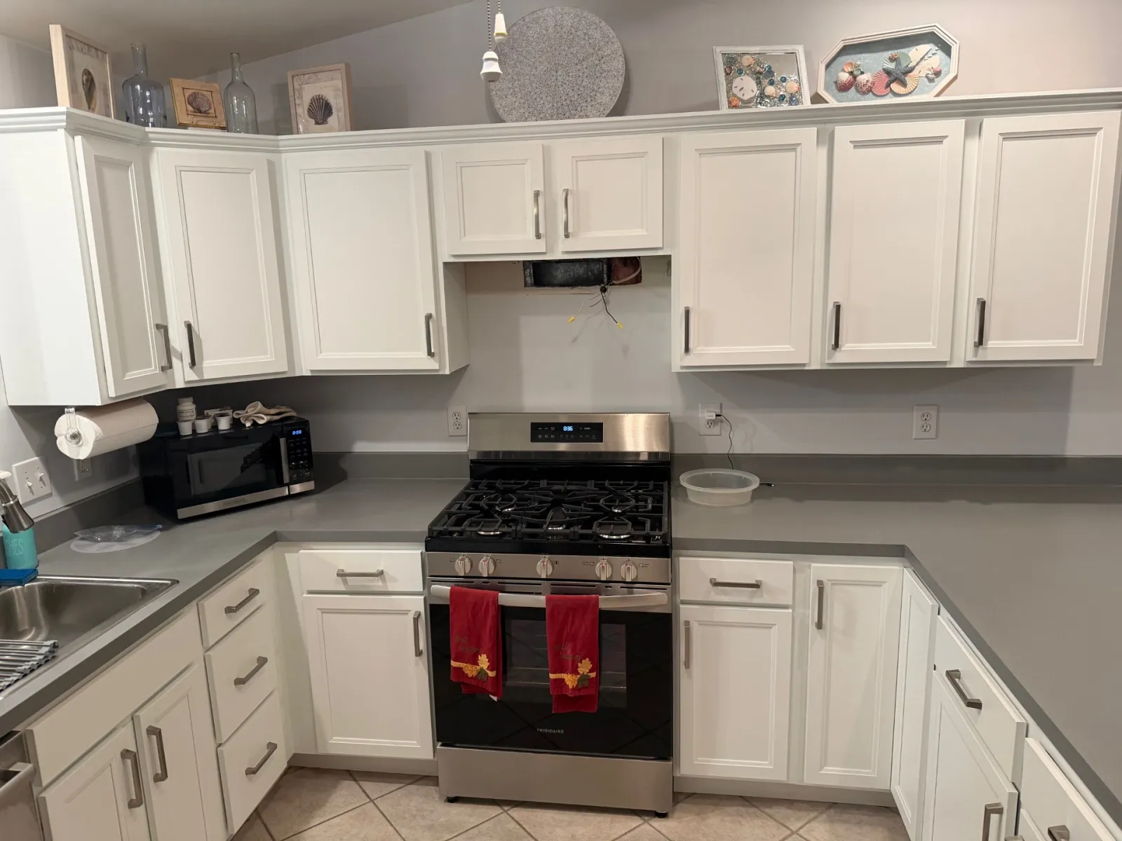 Modern kitchen with white cabinets, stainless steel stove, gray countertops, microwave, and decorative wall art.