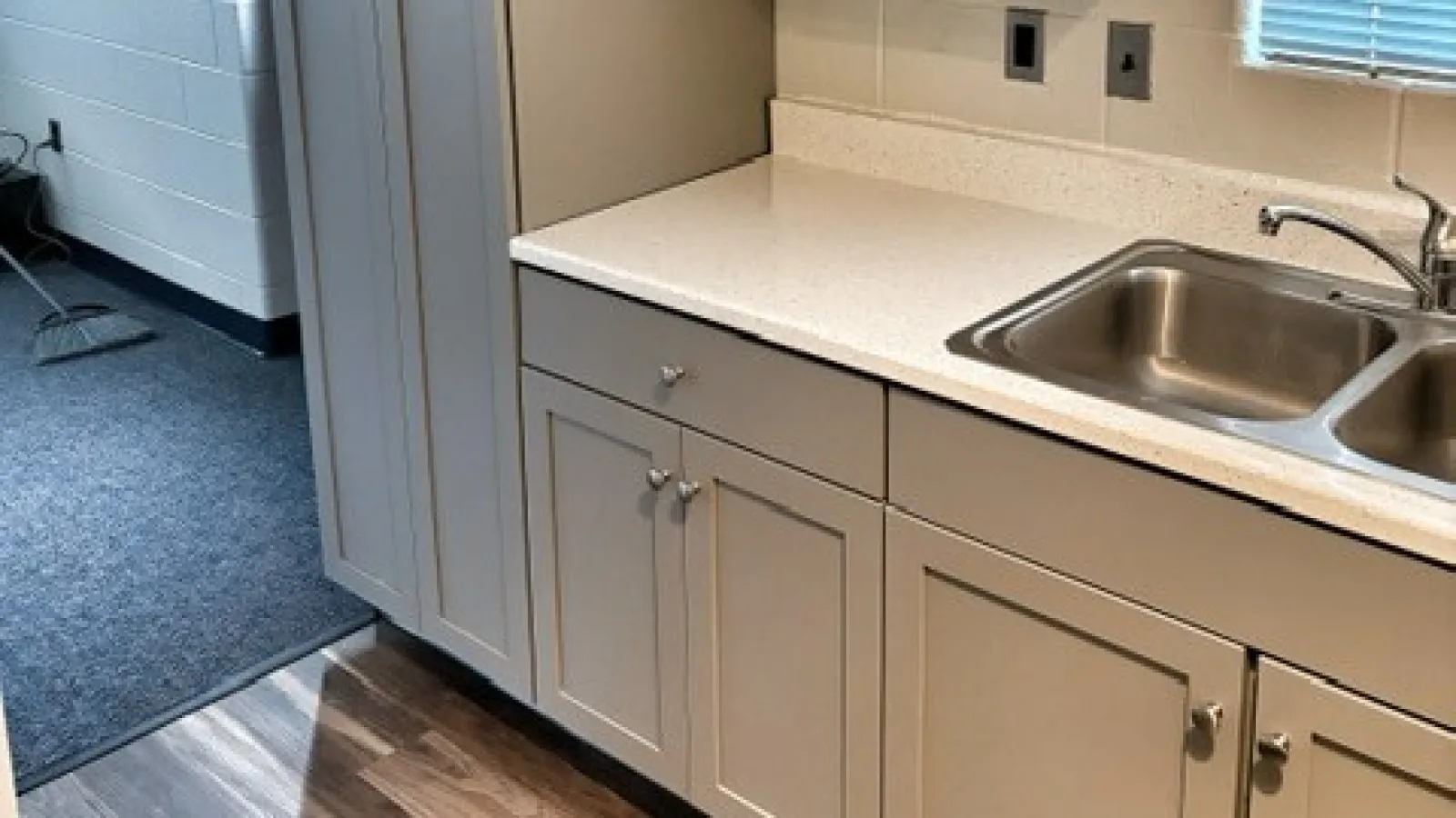 Modern gray kitchen cabinets with white countertop, stainless steel sink, and wood flooring under natural light.