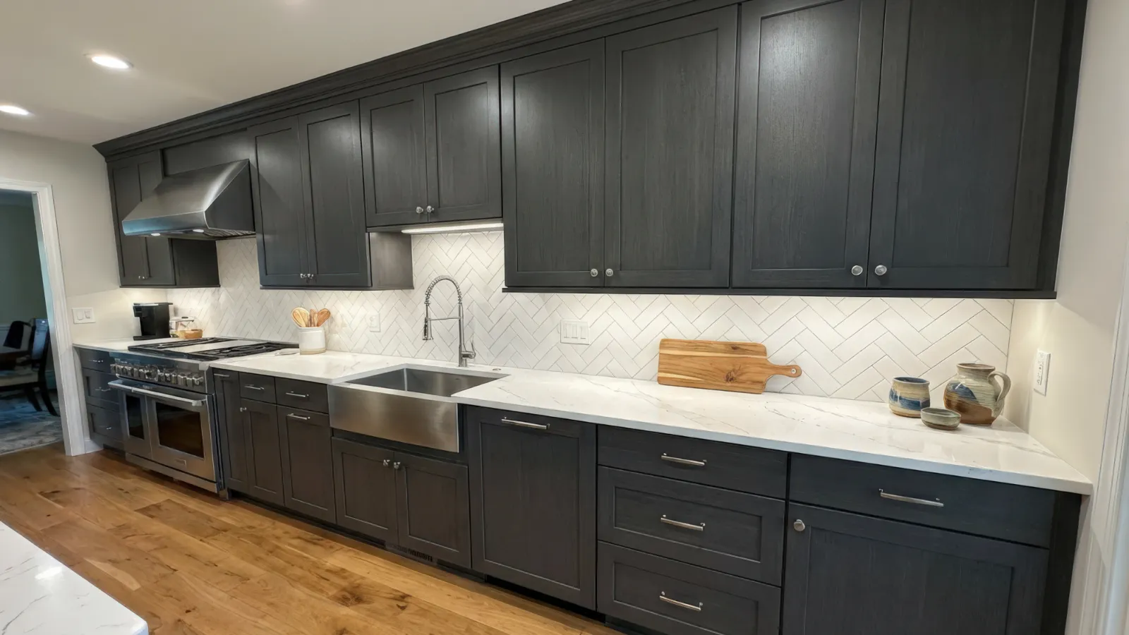 Modern kitchen with dark wood cabinets, white marble countertops, farmhouse sink, and herringbone tile backsplash.