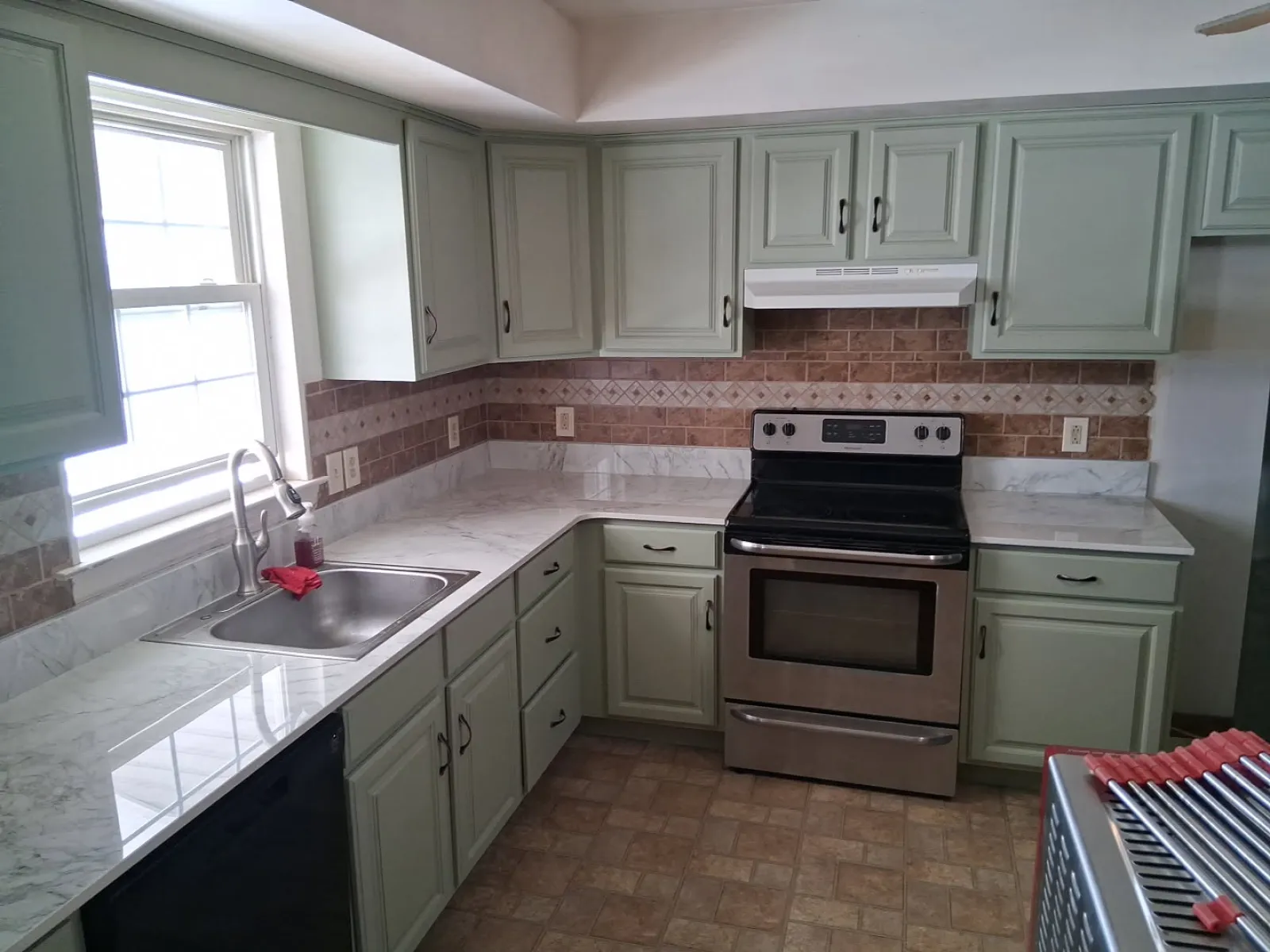 Modern kitchen with light green cabinets, marble countertops, stainless steel stove, and tiled backsplash.