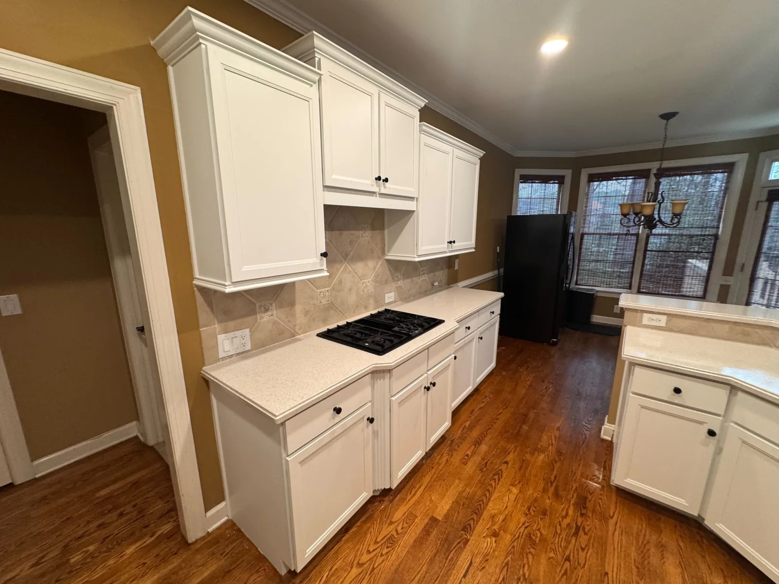 Modern kitchen with white cabinets, beige countertops, hardwood floors, gas stove, and large windows with blinds.
