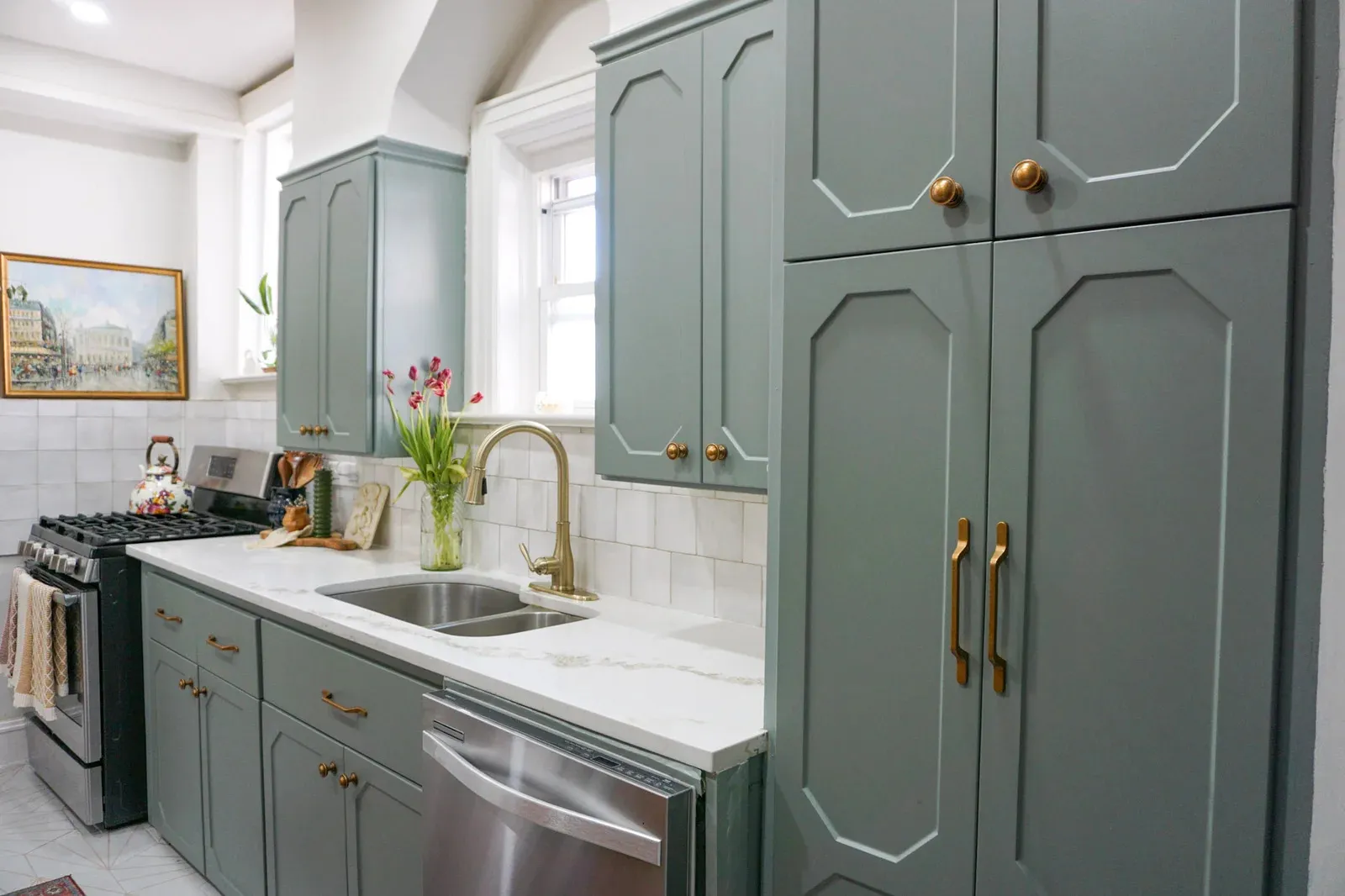 Modern kitchen with green cabinets, white marble countertops, brass fixtures, and stainless steel appliances.