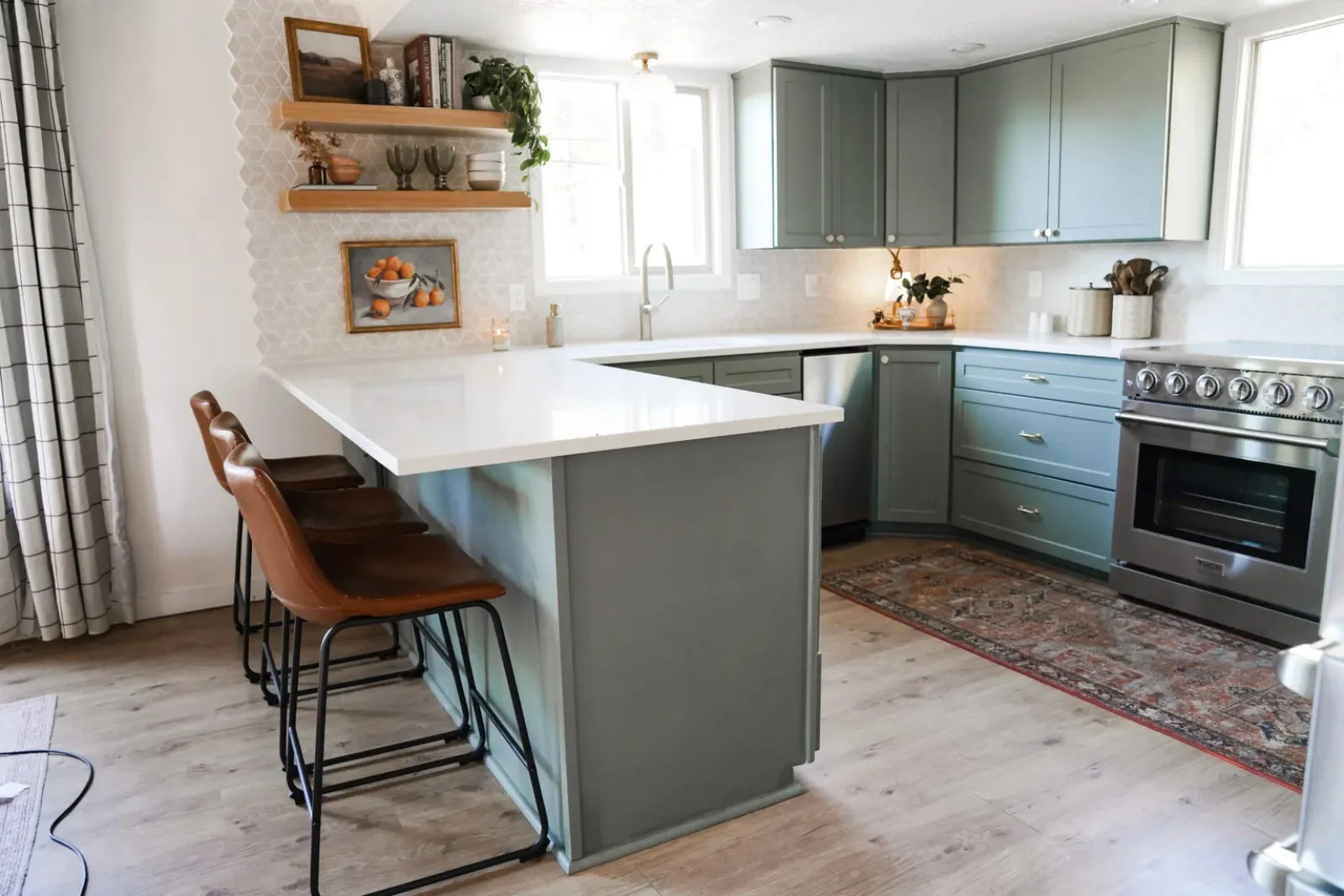 Modern kitchen with gray cabinets, white countertops, leather bar stools, and stainless steel appliances under bright windows