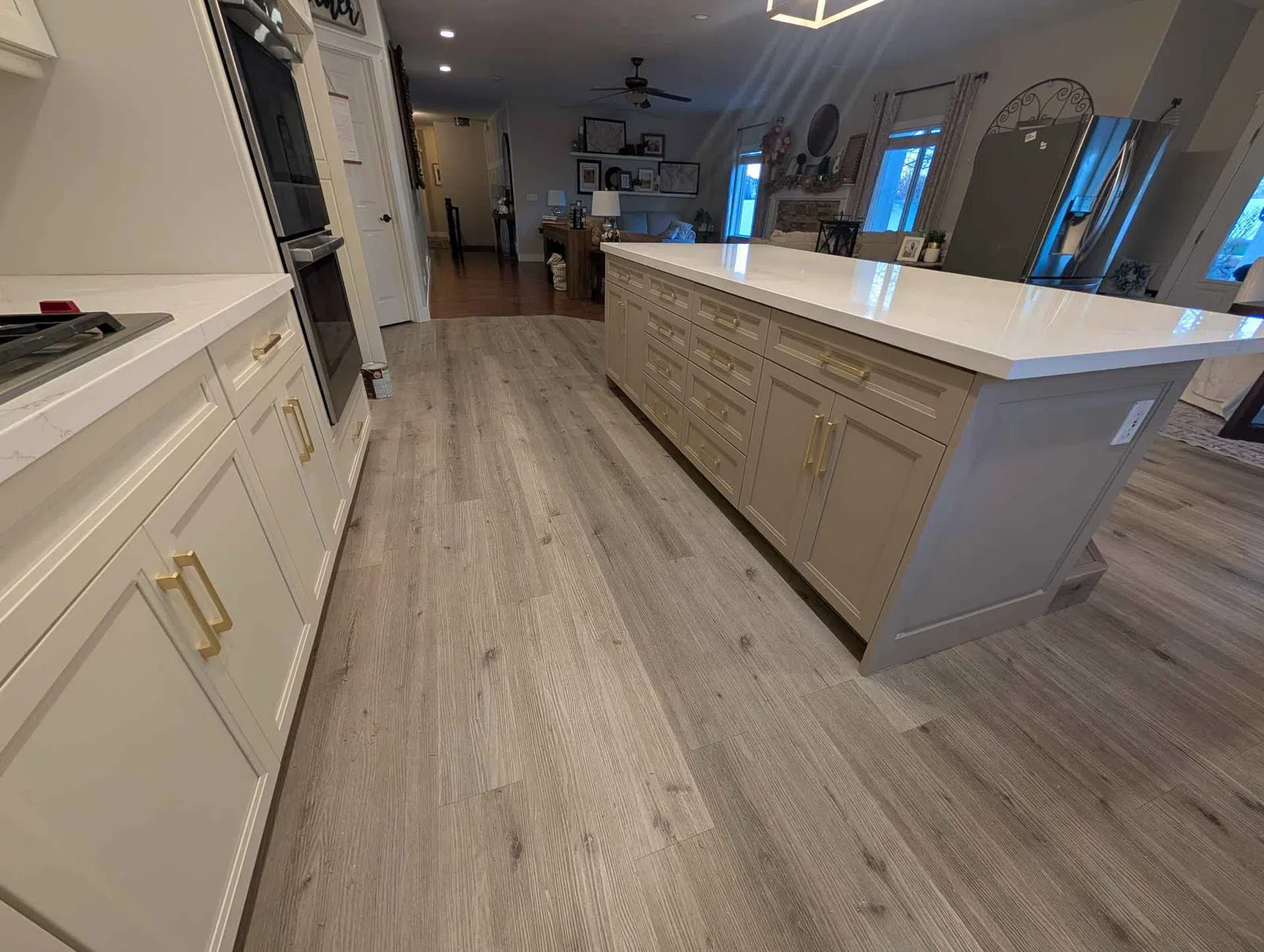 Modern kitchen with beige cabinets, large white island, gold handles, and light gray wood flooring under warm lighting.