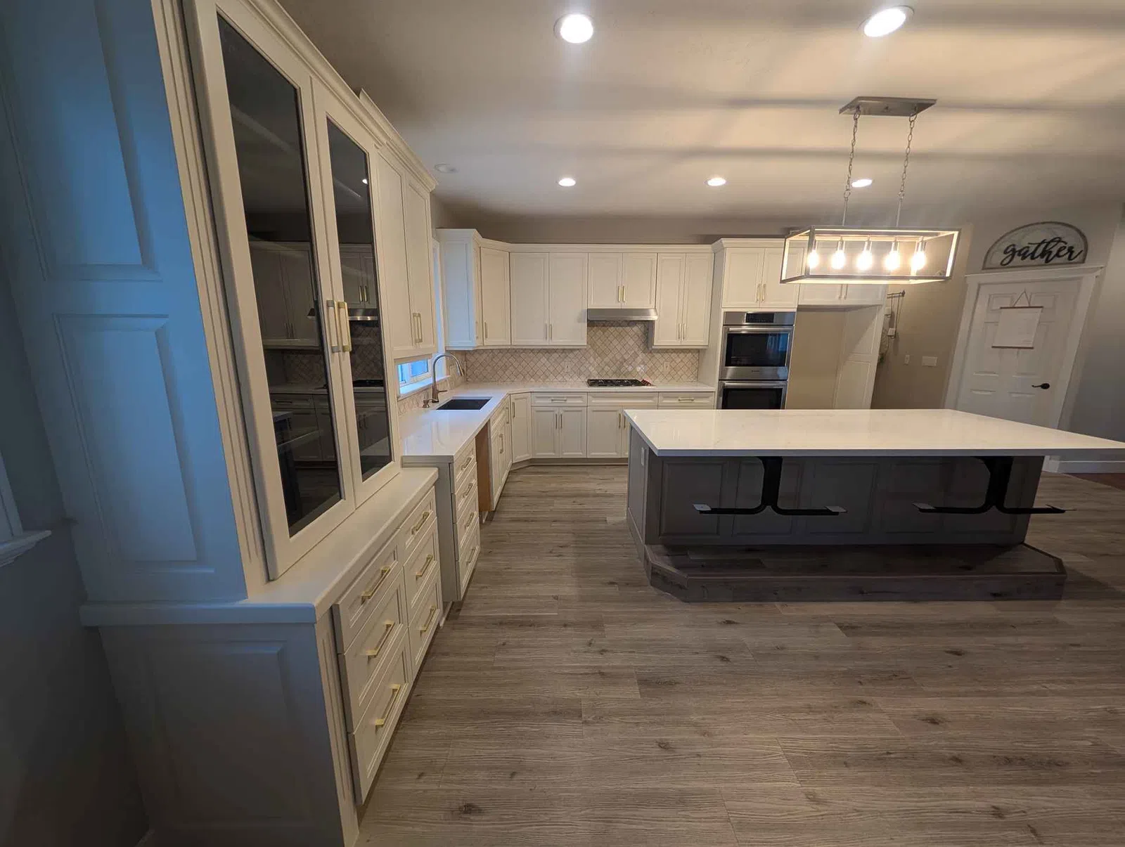 Modern kitchen with white cabinets, large island, wooden floors, and overhead pendant lighting.