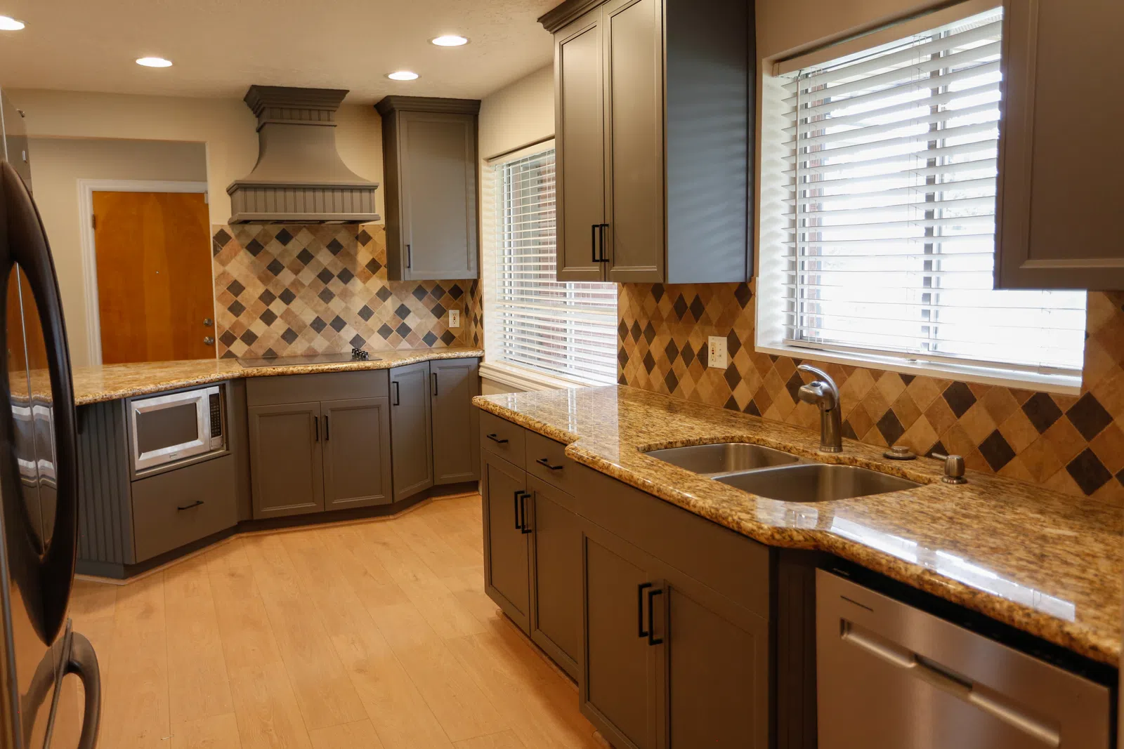 Modern kitchen with granite countertops, gray cabinets, tiled backsplash, stainless steel appliances, and large windows.